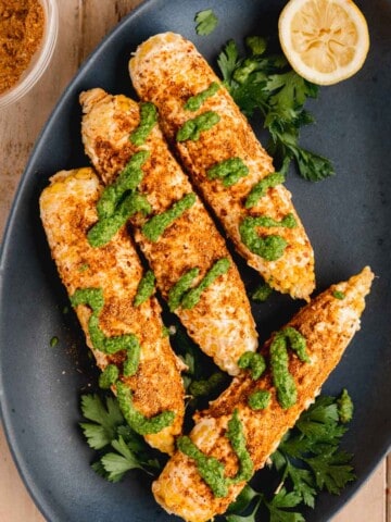 Shawarma Corn on the Cobb topped with garlic mayo, shawarma seasoning and schug sauce on a serving platter.