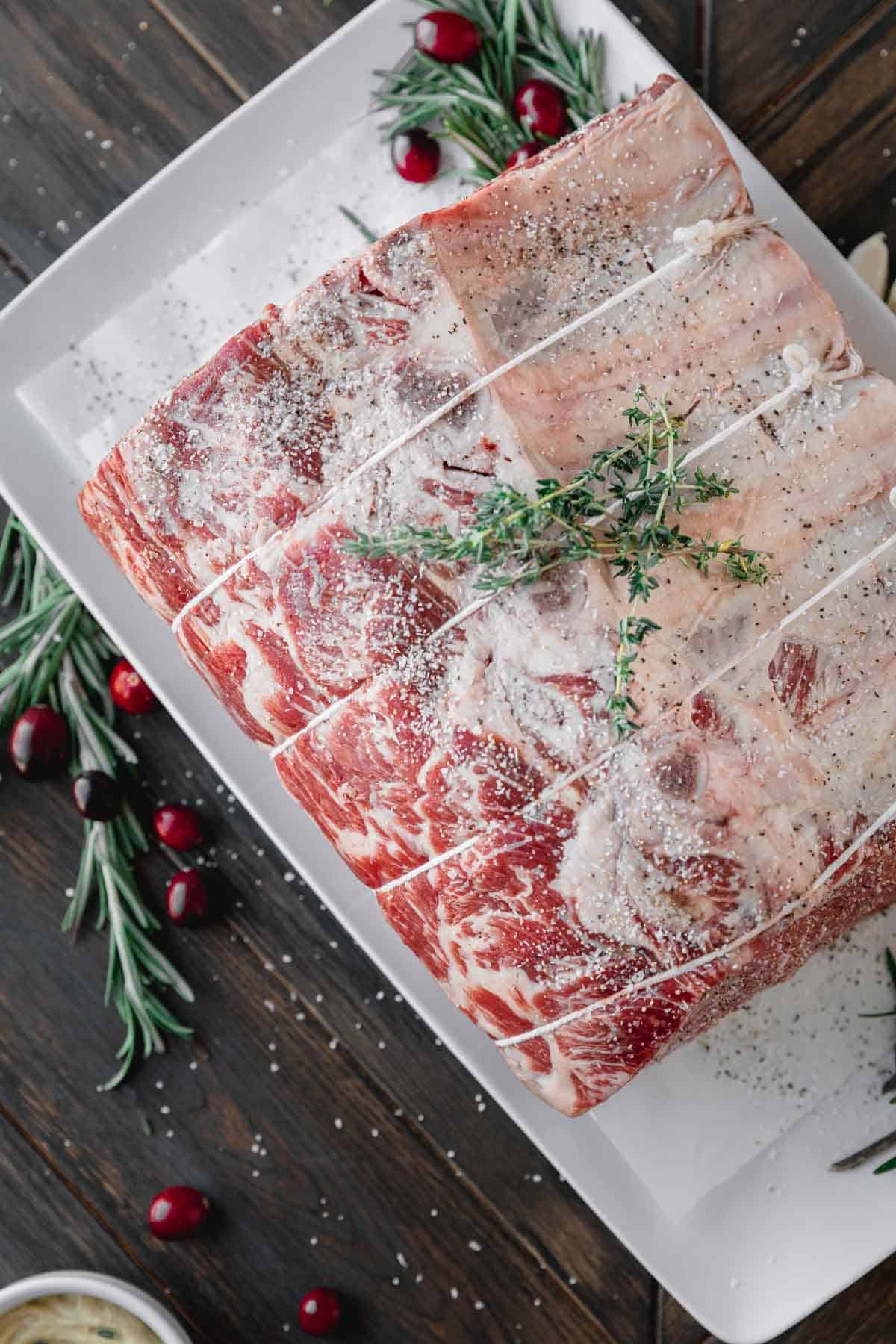 Standing rib roast tied and seasoned on a tray.