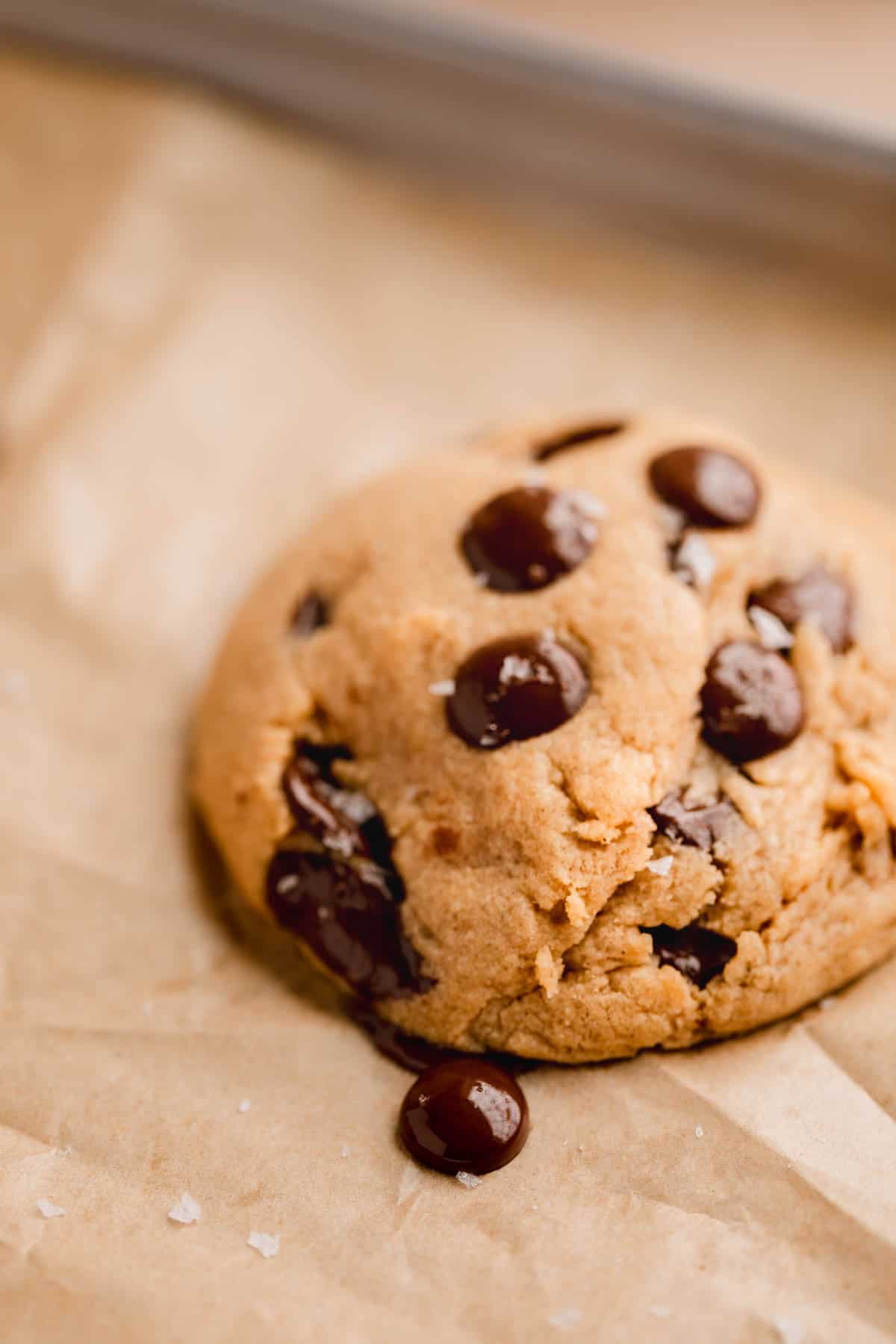 Peanut Butter Chocolate Chip Cookie baked on a sheet tray lined with parchment paper, topped with flaky sea salt. 