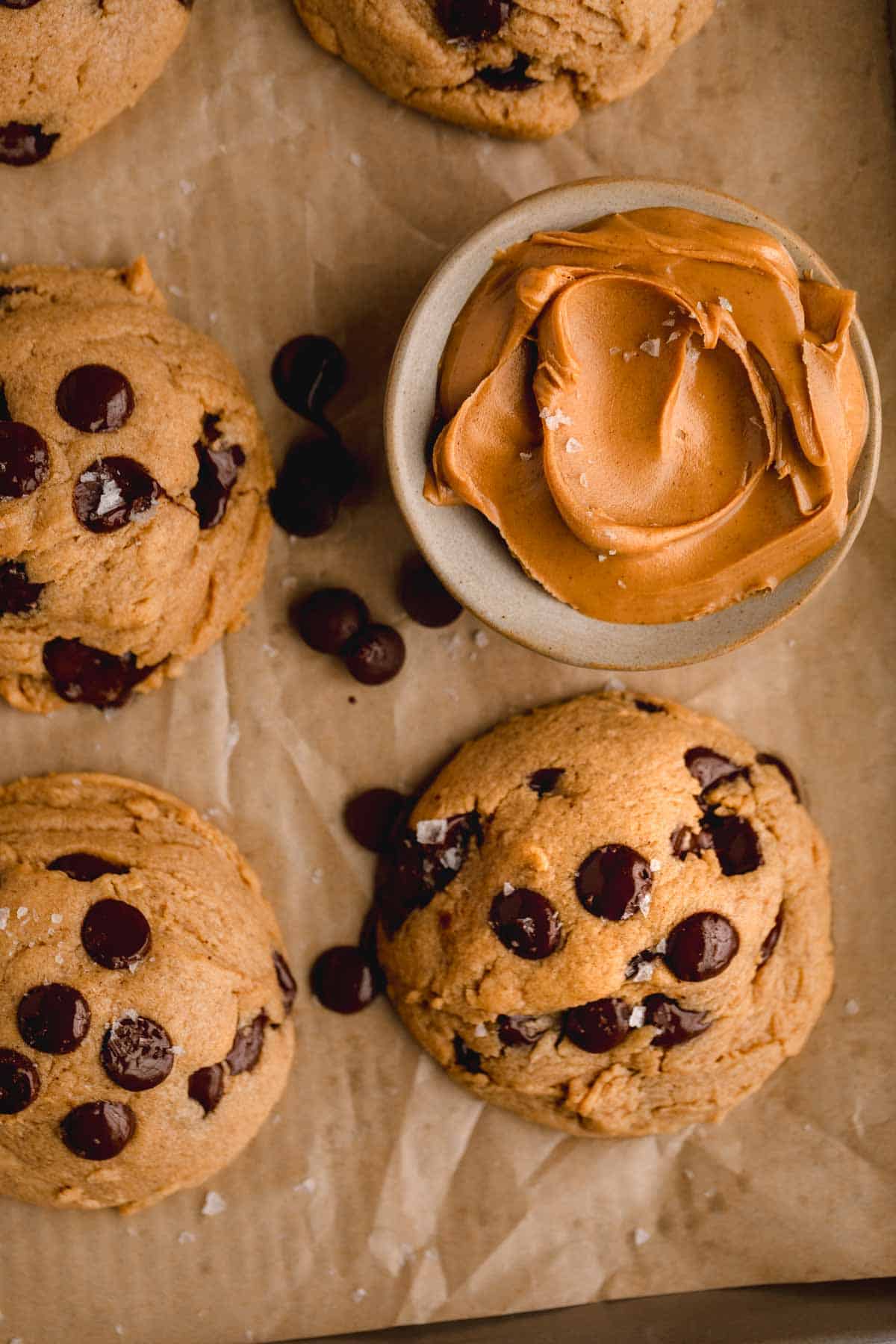 Chocolate Chip Peanut Butter Cookies on a tray with parchment paper, a dish of peanut butter and flaky sea salt. 