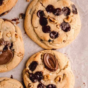 Chocolate Chip Walnut Cookies topped with flaky sea salt on a board with parchment paper.