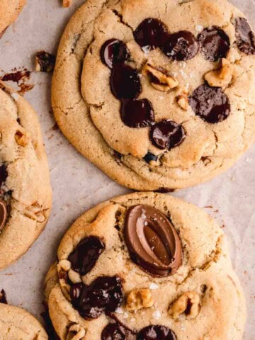 Chocolate Chip Walnut Cookies topped with flaky sea salt on a board with parchment paper.