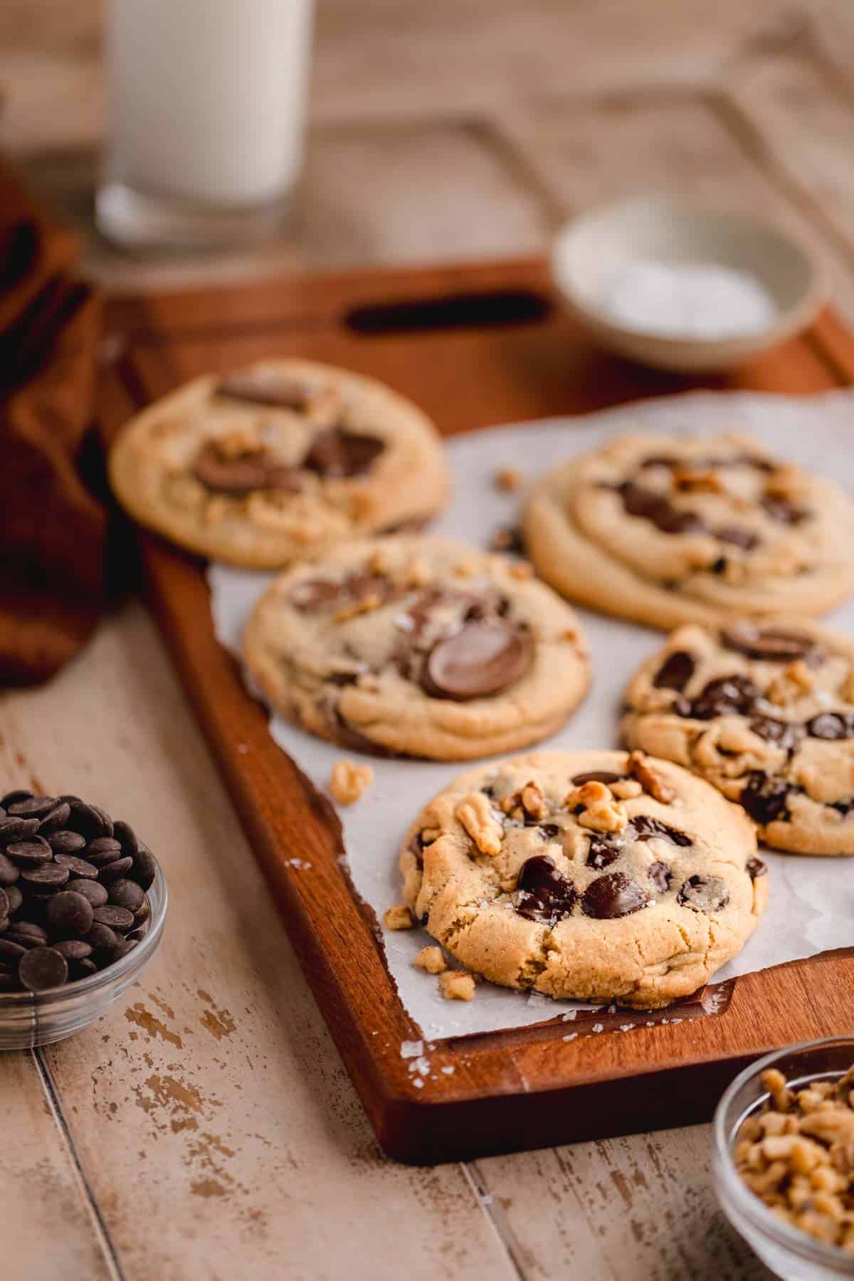 Walnut Chocolate Chip Cookies topped with flaky sea salt and a parchment lined cutting board. 