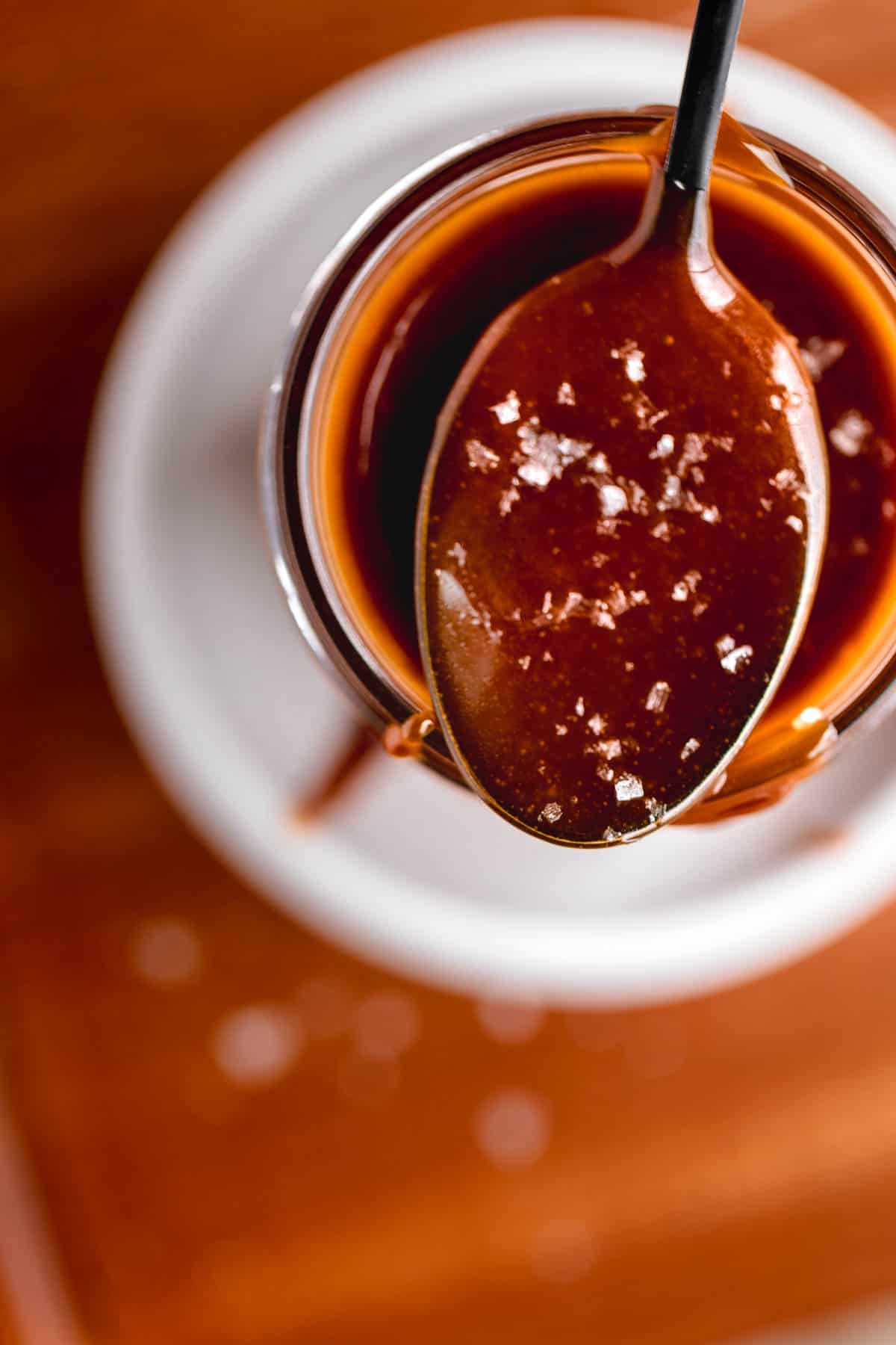 Quick Caramel Sauce on a spoon topped with flaky sea salt. 