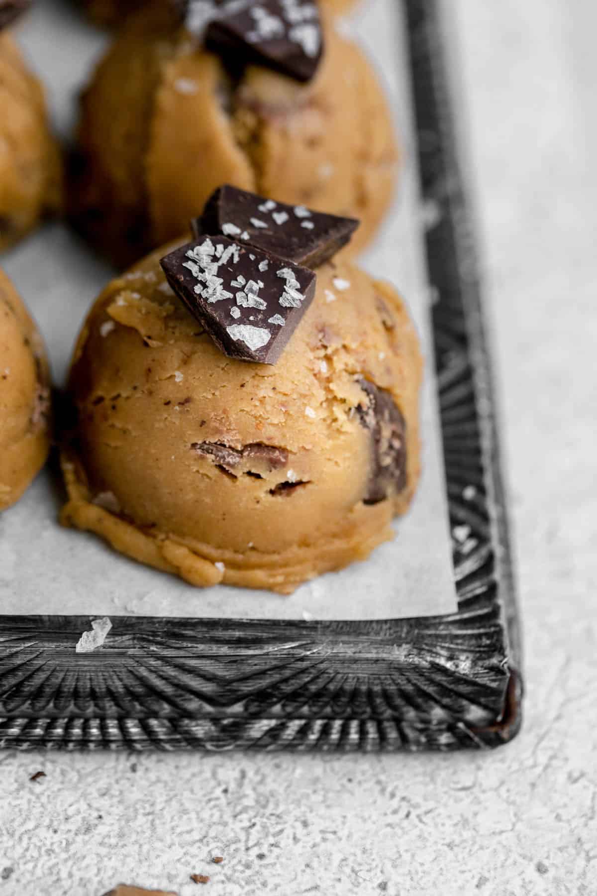 Brown Butter Toffee Chocolate Chip Cookie dough scooped into balls on a tray, topped with chocolate and salt.