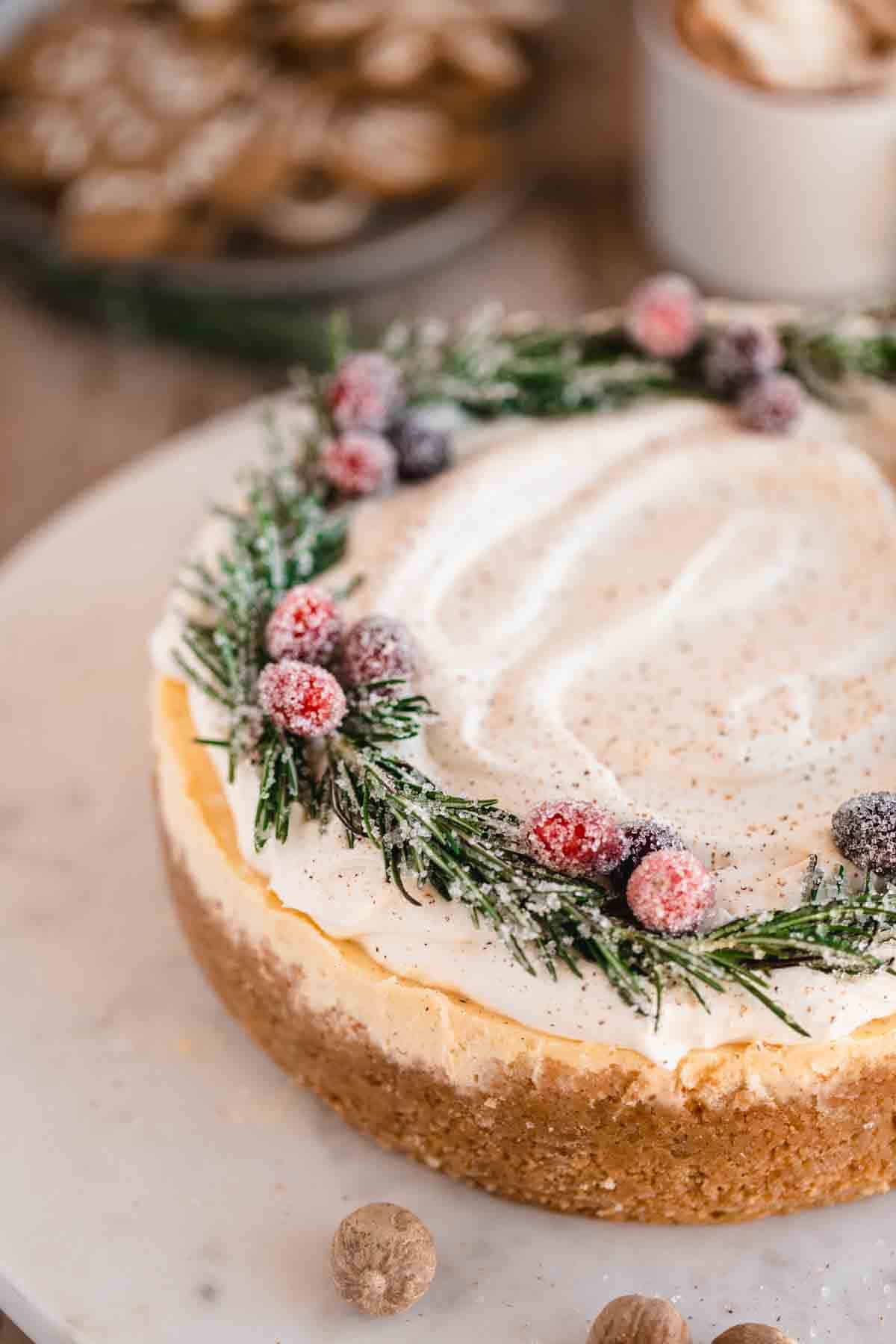 Eggnog Cheesecake topped with whipped cream, decorated with sugared cranberries and sugared rosemary. 