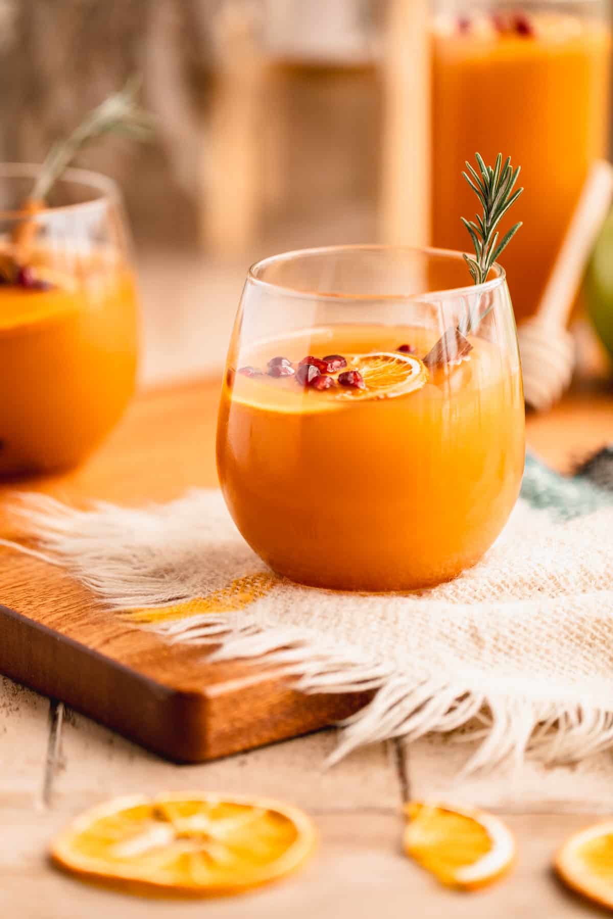 Mulled Apple Cider in a glass with dried orange slices, rosemary and pomegranate.