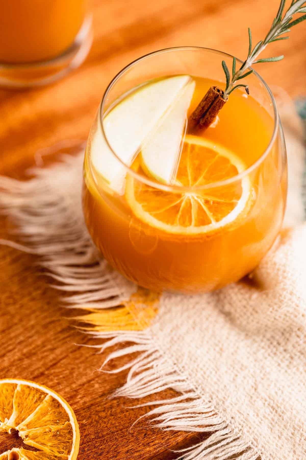 Apple cider garnished with apple slices, cinnamon and dried orange.