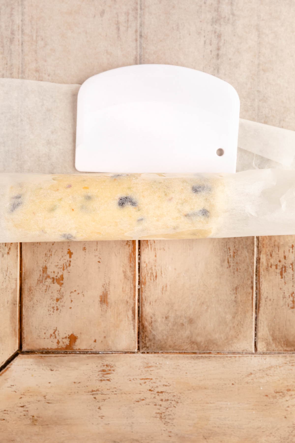 Shortbread cookies being rolled into a log with parchment paper and a bench scraper.
