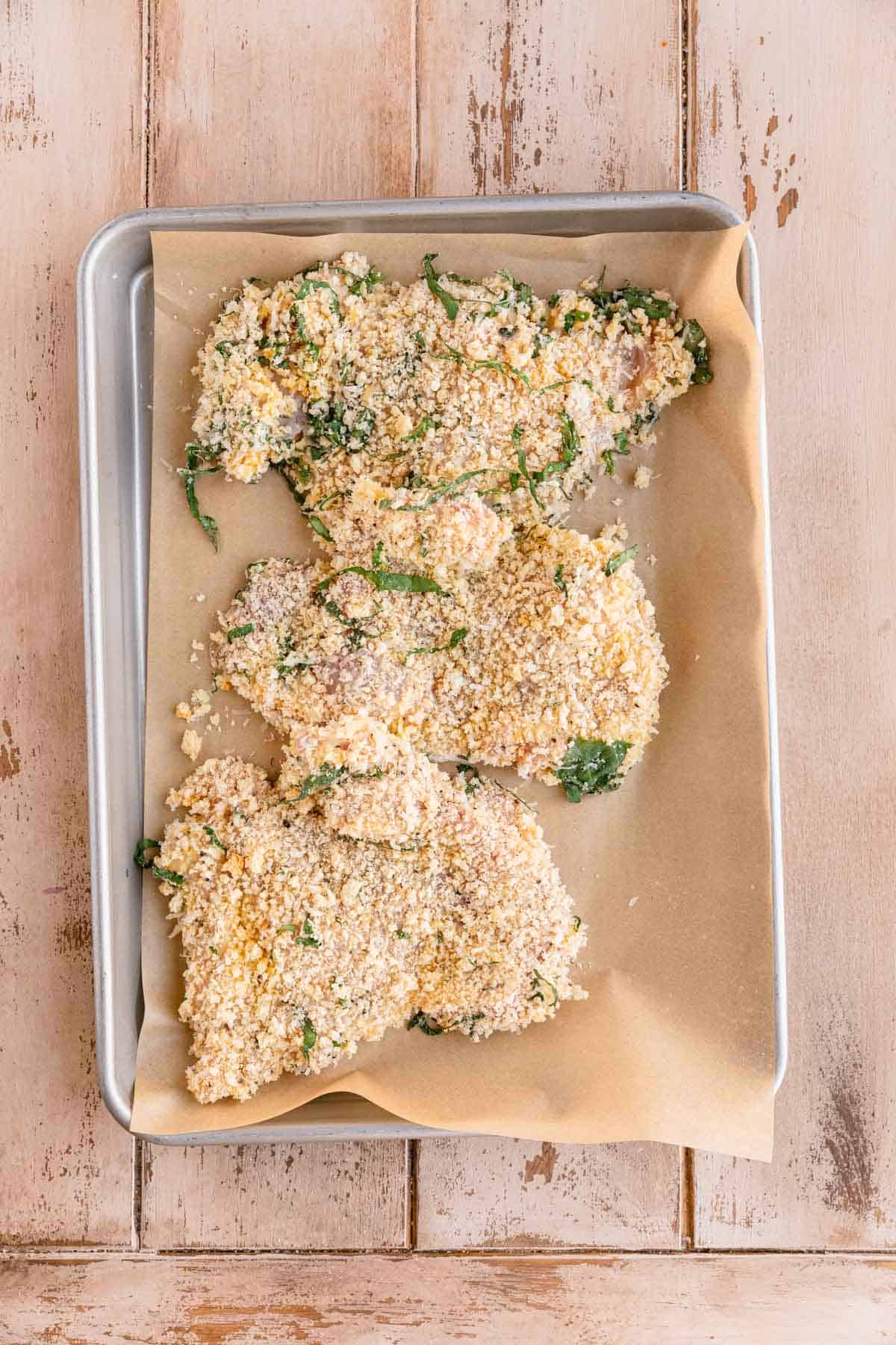 Chicken thighs breaded in a parmesan panko mixture sitting on a sheet tray.