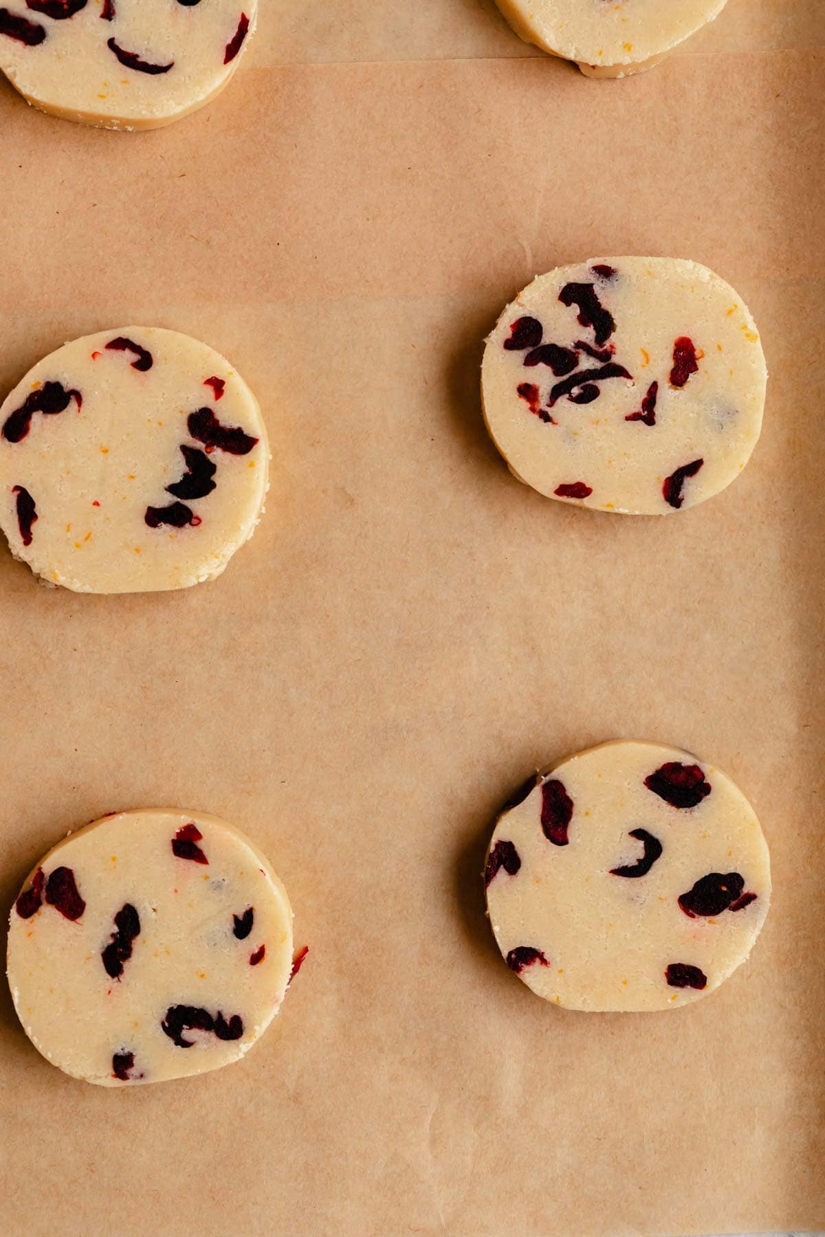 Cranberry Orange Shortbread Cookies sliced on a pan with parchment paper.