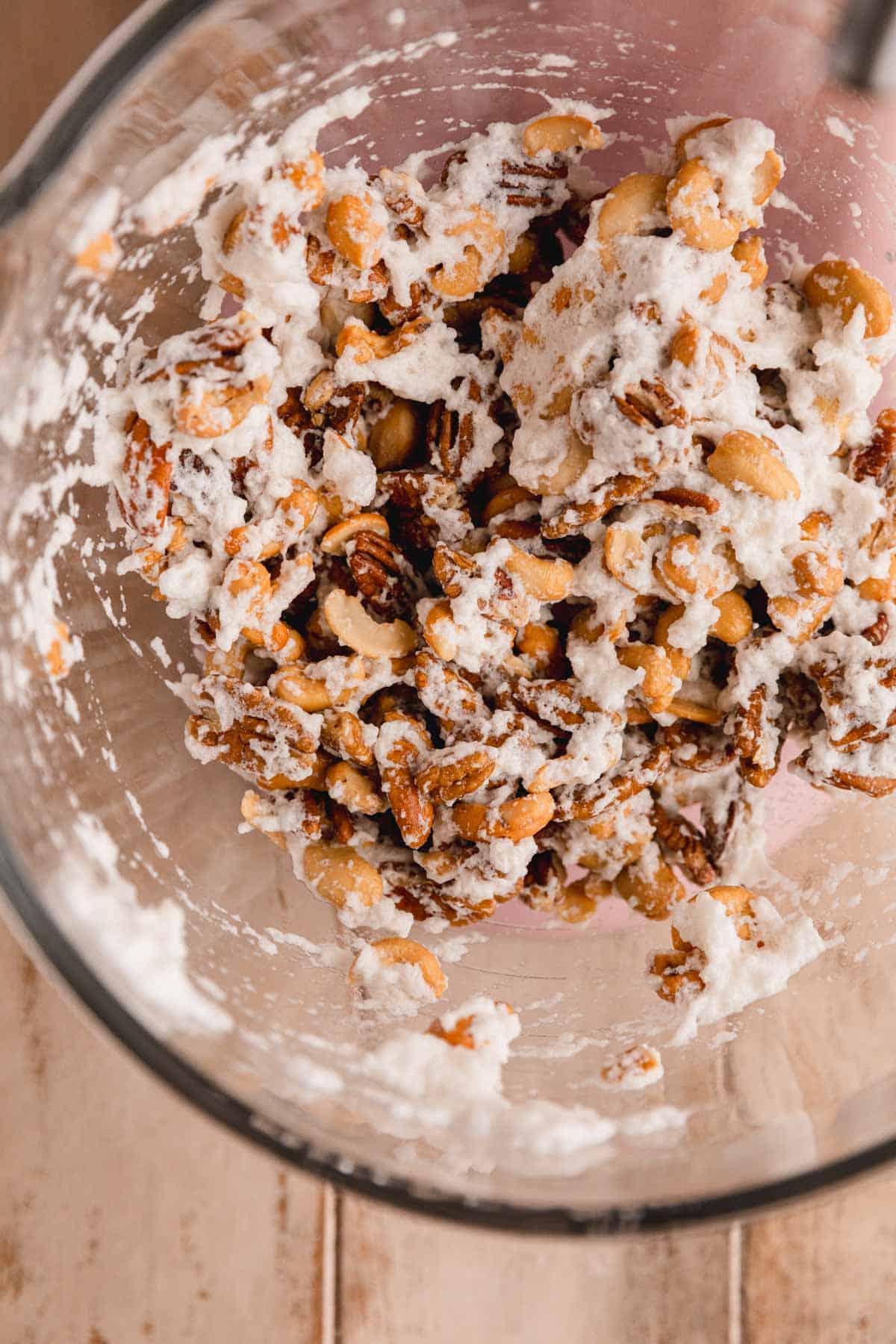 Pecans and cashews mixed with stiff egg whites in a bowl.