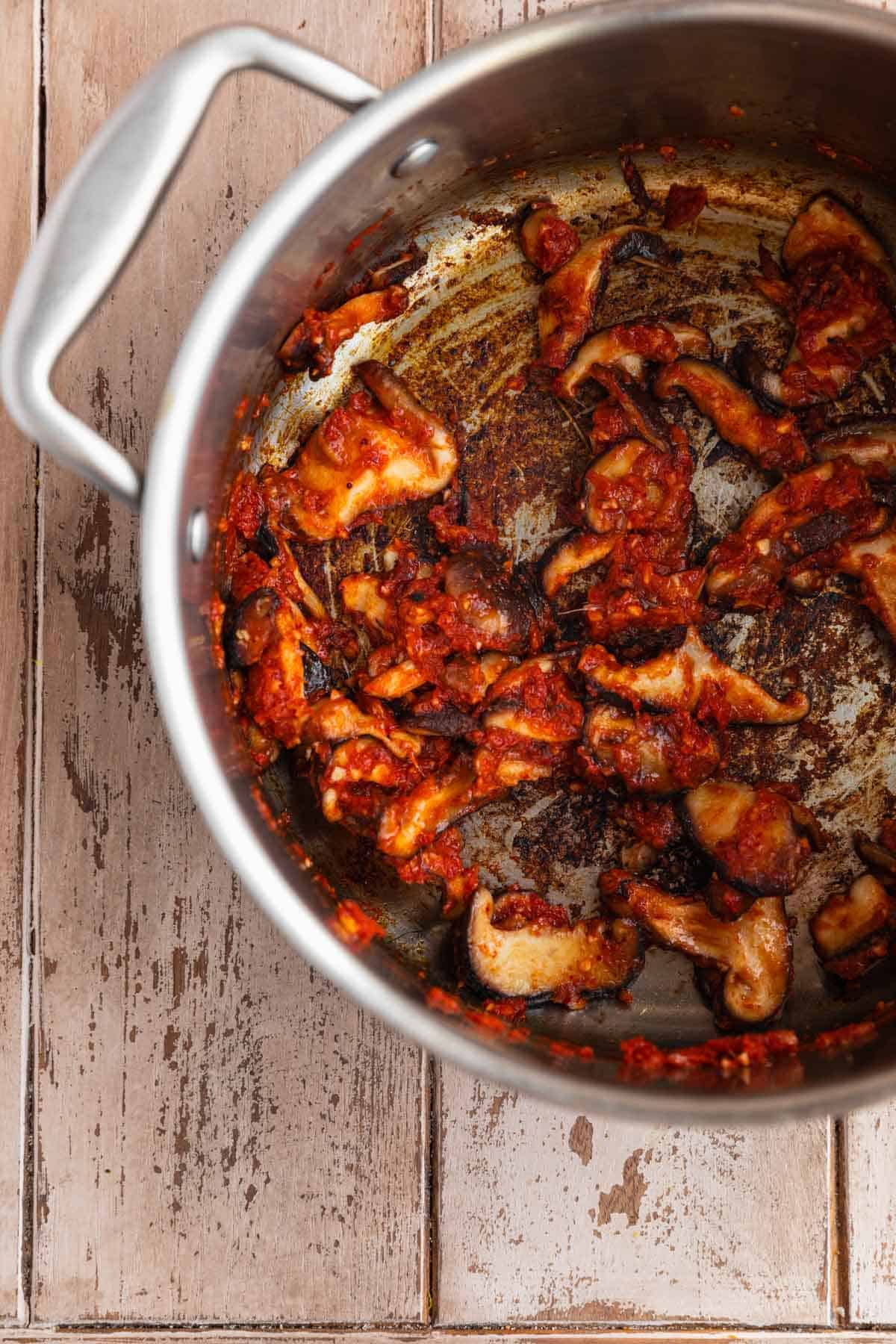 Mushrooms being sauteed with red curry paste, ginger, garlic and lemongrass in a pot. 