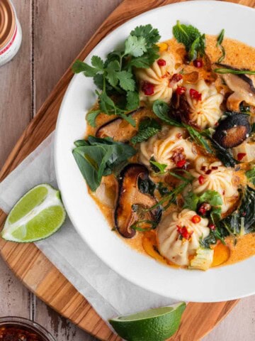 Red Curry Dumpling Soup with cilantro, limes and chili oil sitting on a cutting board.