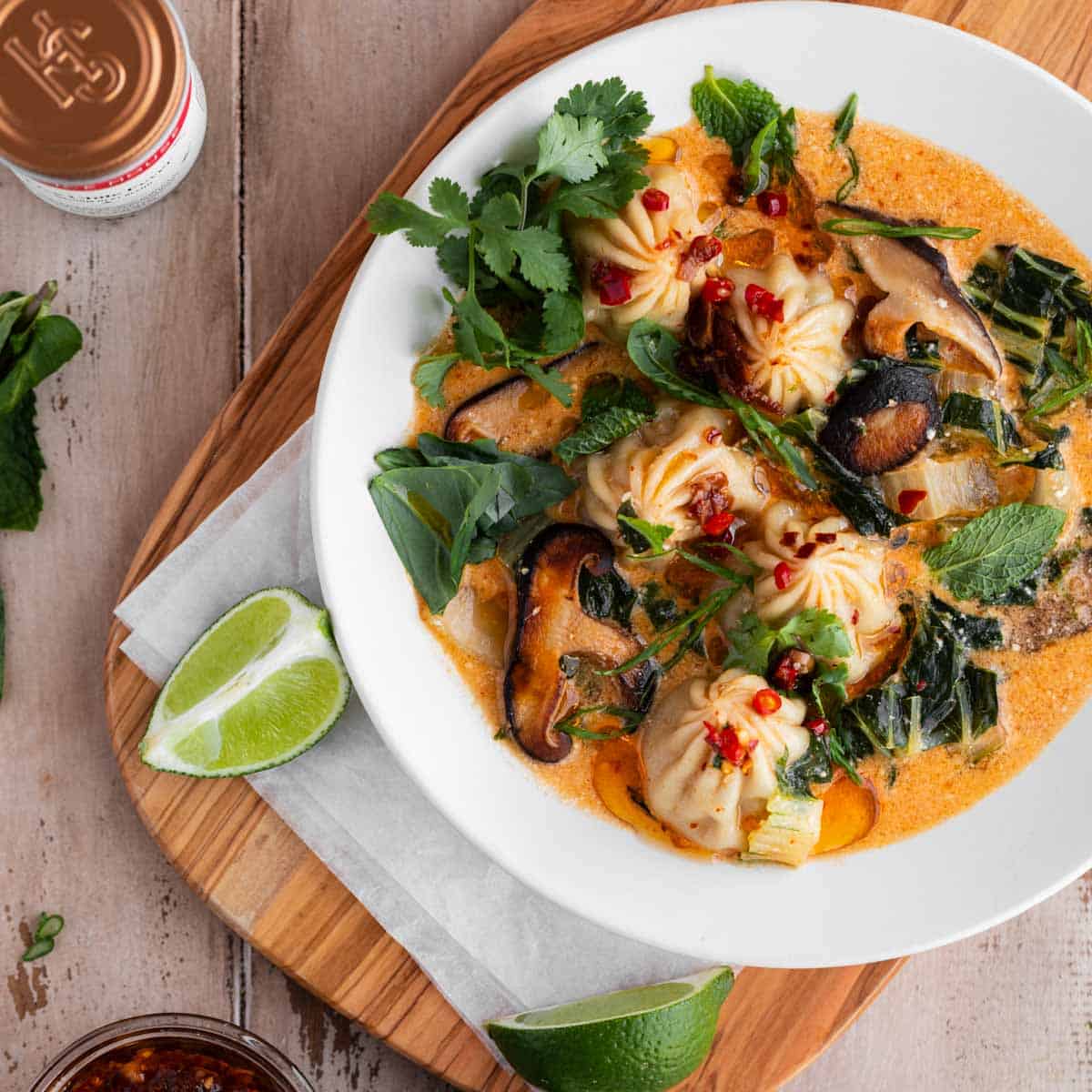 Red Curry Dumpling Soup with cilantro, limes and chili oil sitting on a cutting board.