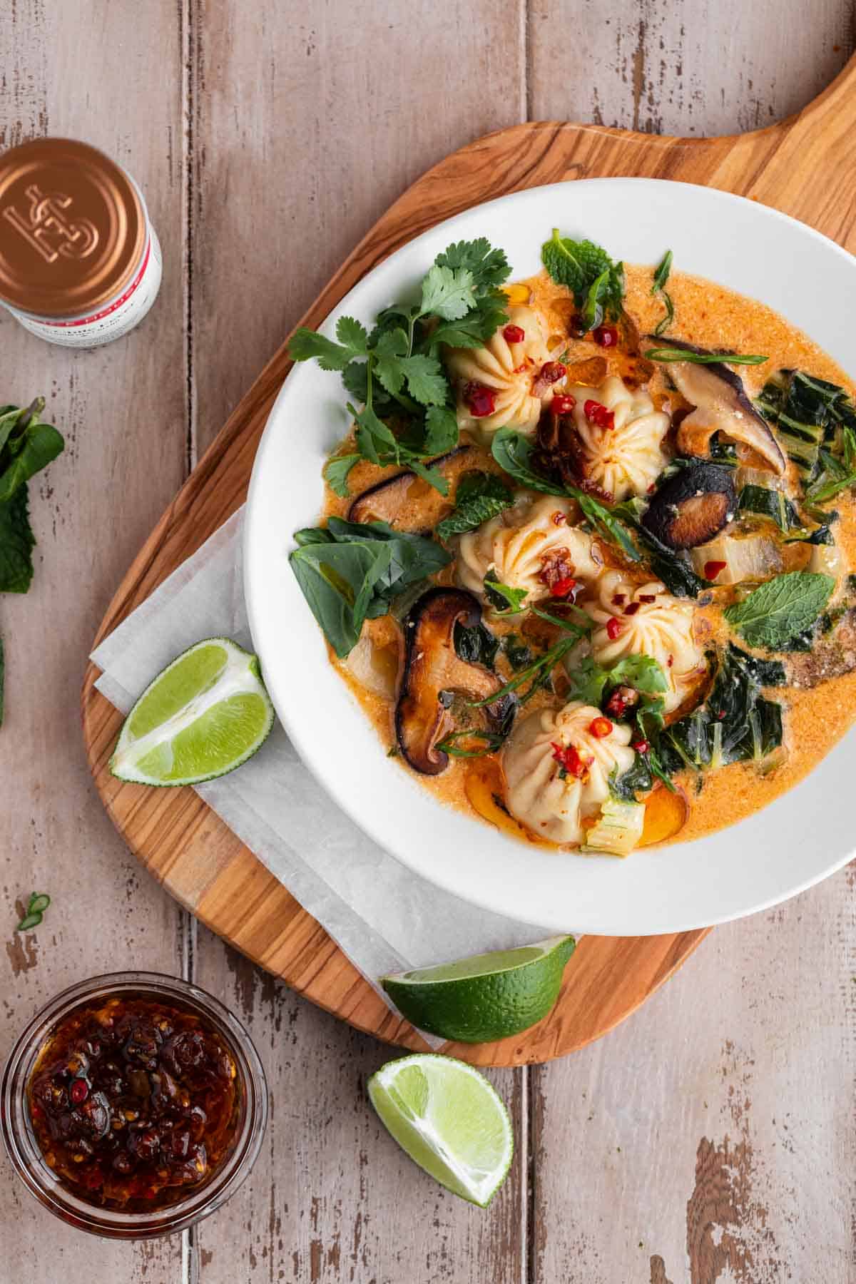 Red Curry Dumpling Soup with cilantro, limes and chili oil sitting on a cutting board. 