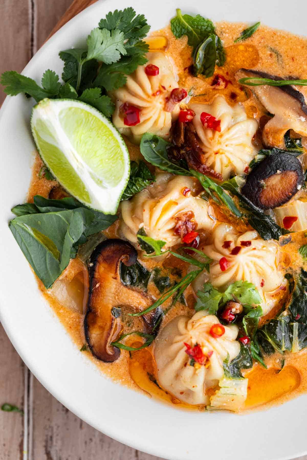 Red Curry Dumpling Soup in a bowl with fresh herbs, a lime wedge and thai chiles. 