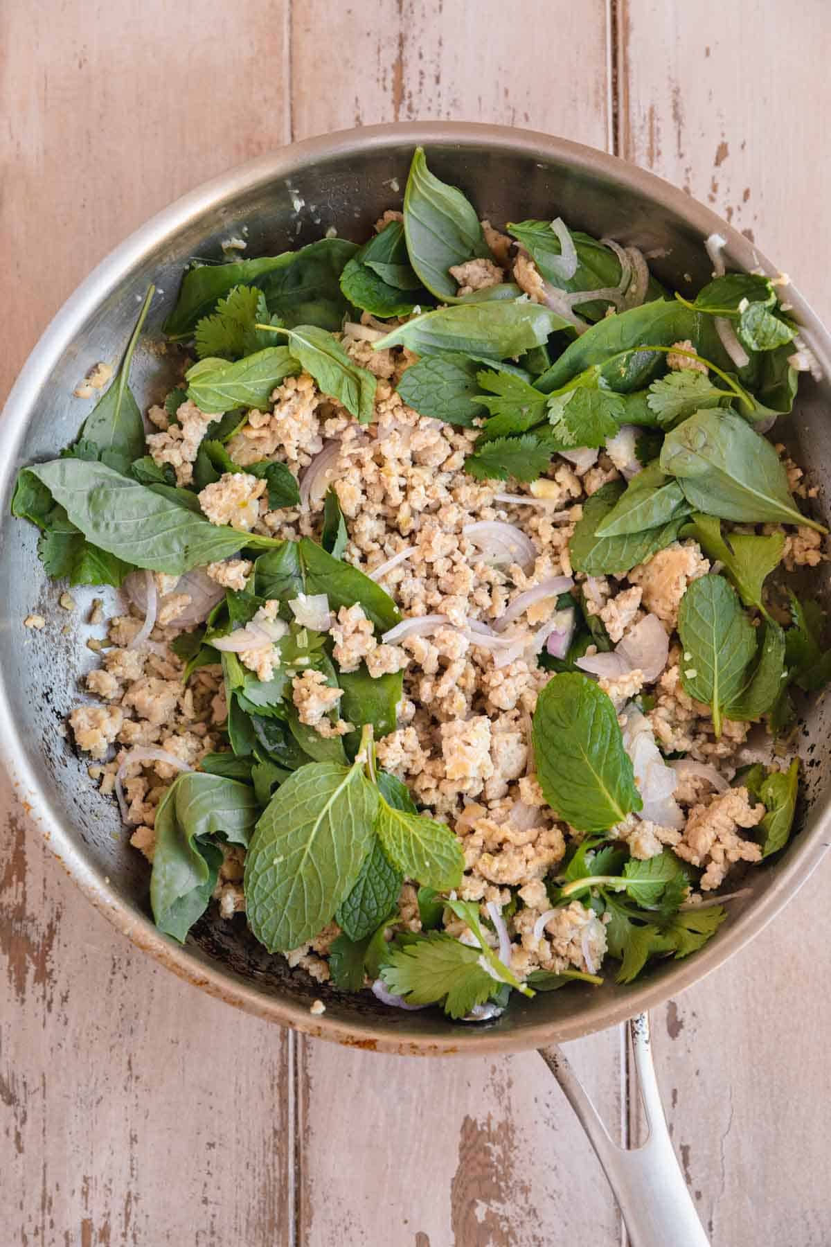 Ground chicken in a skillet with herbs and fish sauce. 