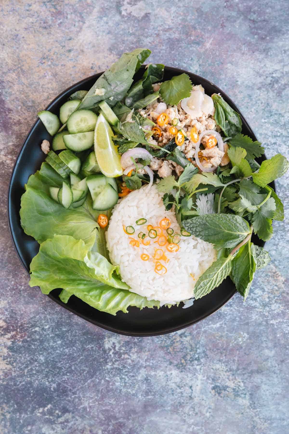 Chicken Larb served with mint, basil, cilantro, jasmine rice, Thai chiles and a lime wedge. 