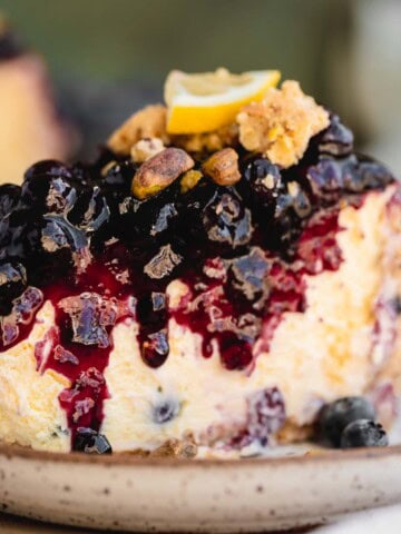 A slice of Lemon Blueberry Cheesecake with pistachio crumble on top.