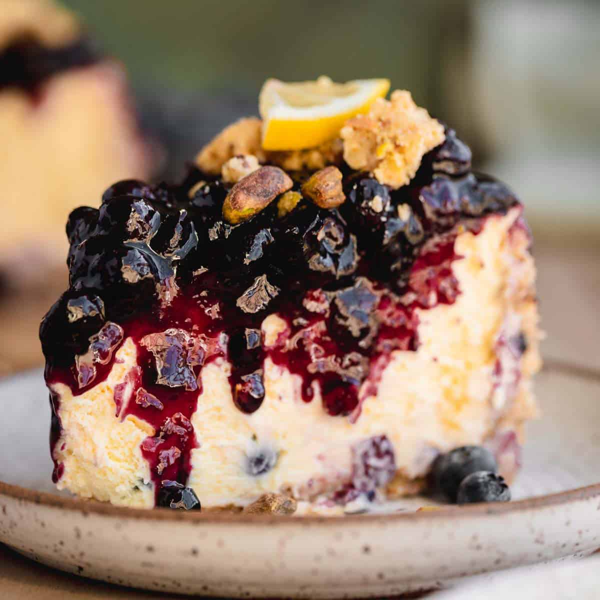 A slice of Lemon Blueberry Cheesecake with pistachio crumble on top.