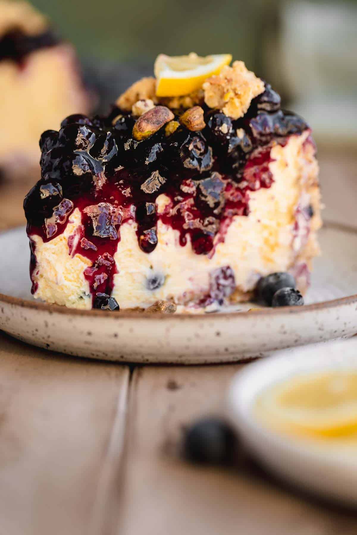 A slice of Lemon Blueberry Cheesecake with pistachio crumble on top.