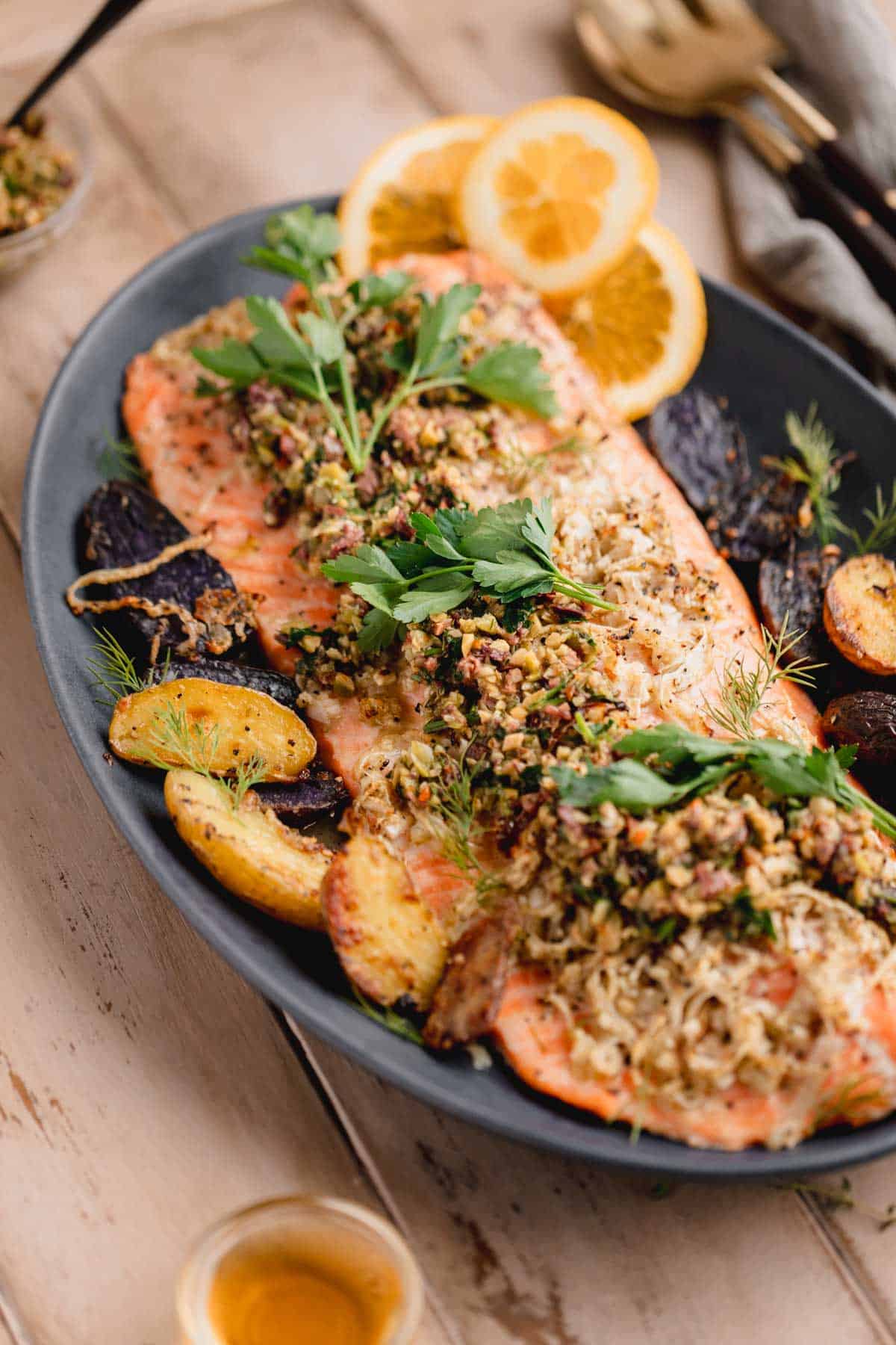 Mediterranean Citrus Roasted Salmon with Olive Relish on a serving platter with orange slices and fingerling potatoes. 