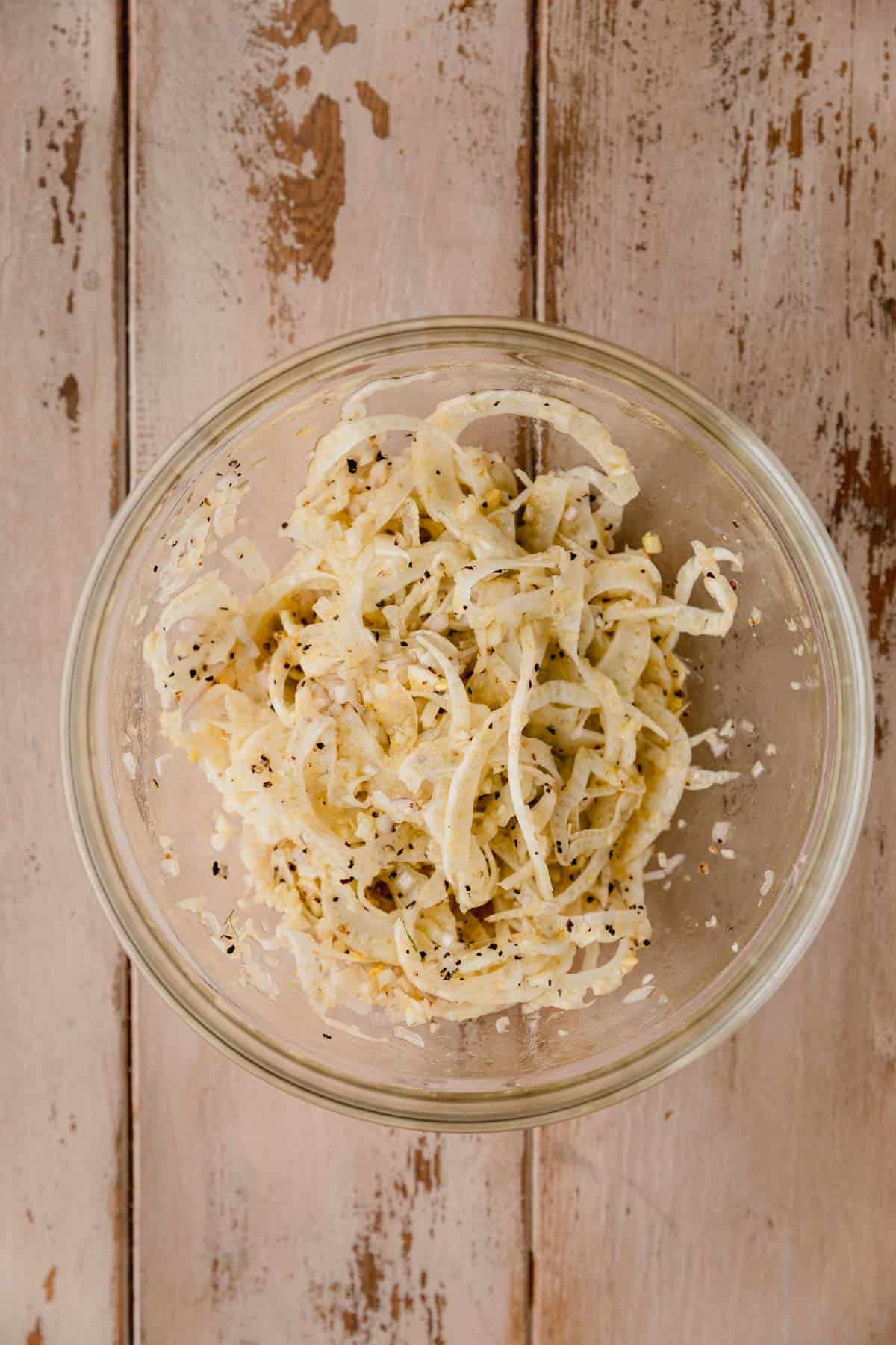 Fennel, garlic, salt, pepper and olive oil mixed in a bowl.