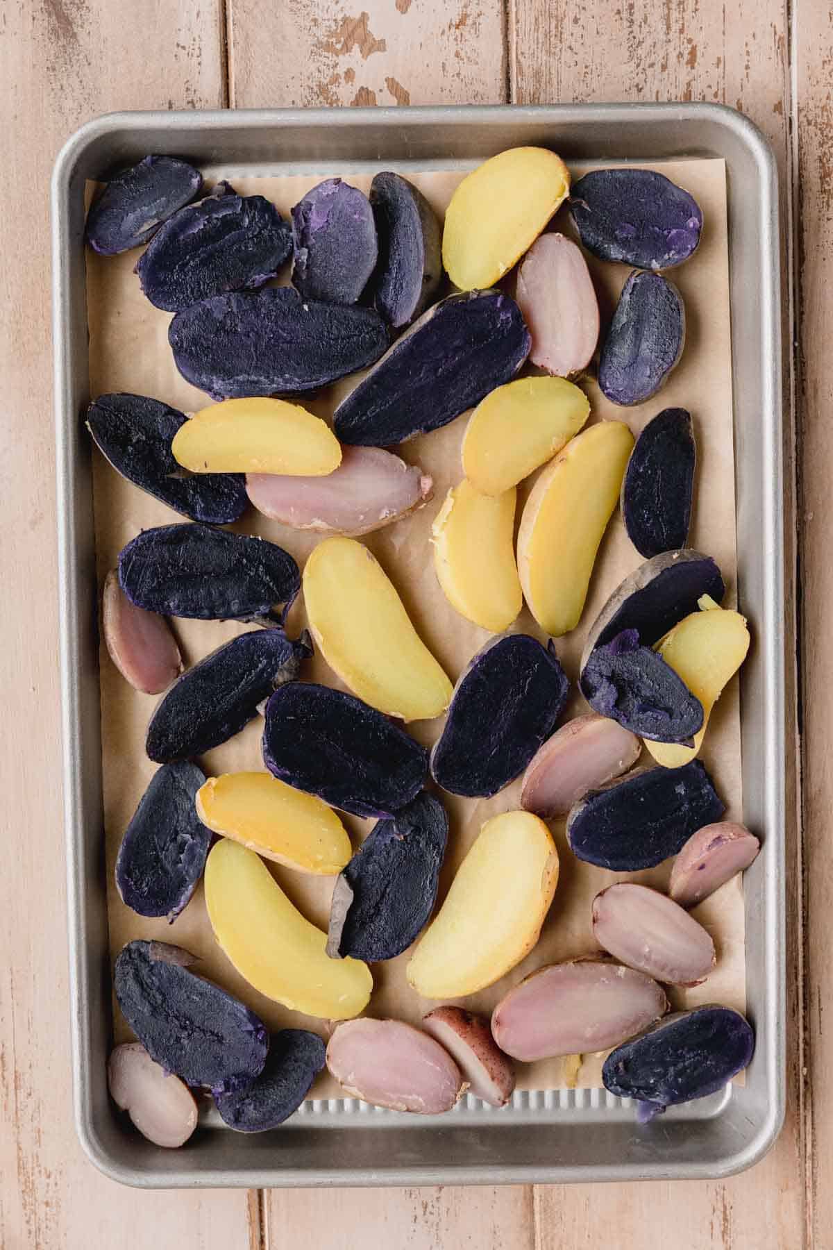 Boiled fingerling potatoes that have been sliced in half on a sheet tray.