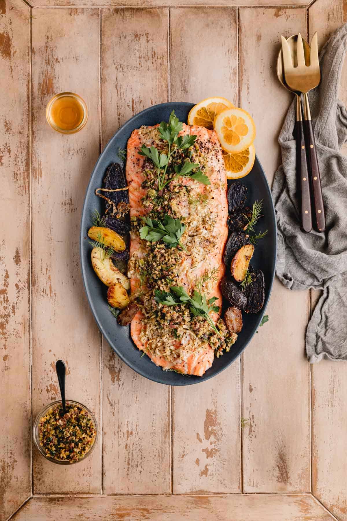 Mediterranean Citrus Roasted Salmon with olive relish on a serving platter with serving utensils and a napkin to the side. 
