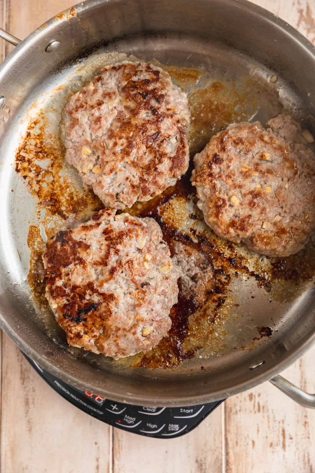 Cooked pork burgers in a skillet.