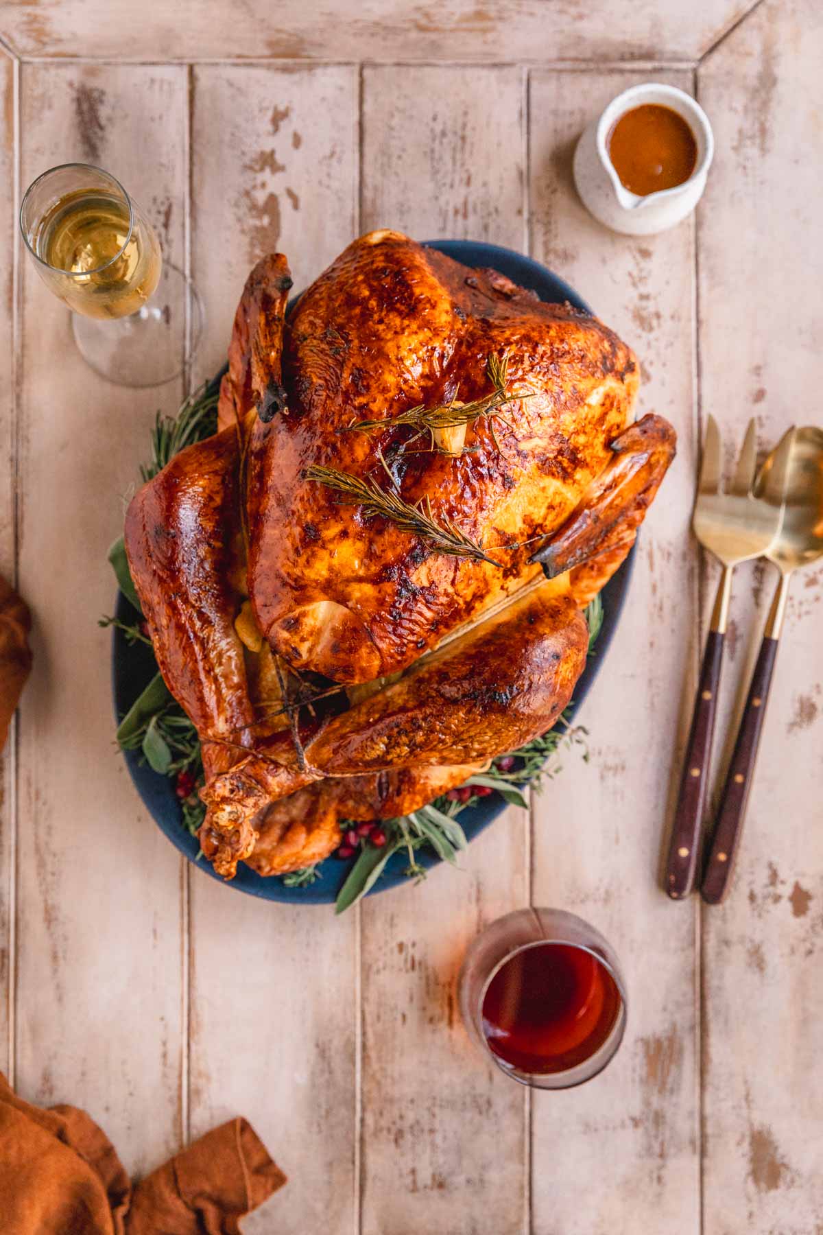 Dry brined roast turkey on a platter with herbs and pomegranate set on a table with wine and gravy.