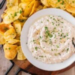 French Onion Dip with Truffle Oil topped with chives on a serving platter with potato chips.