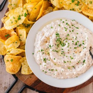 French Onion Dip with Truffle Oil topped with chives on a serving platter with potato chips.