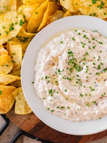 French Onion Dip with Truffle Oil topped with chives on a serving platter with potato chips.