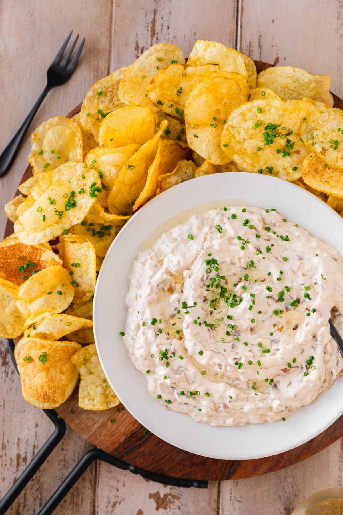 French Onion Dip with Truffle Oil in a bowl surrounded by potato chips and garnished with chives.