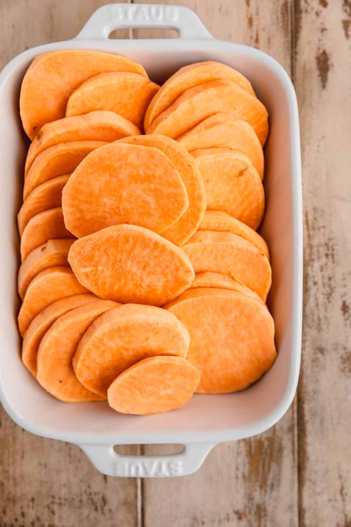 Peeled and sliced sweet potatoes layered in a baking dish.