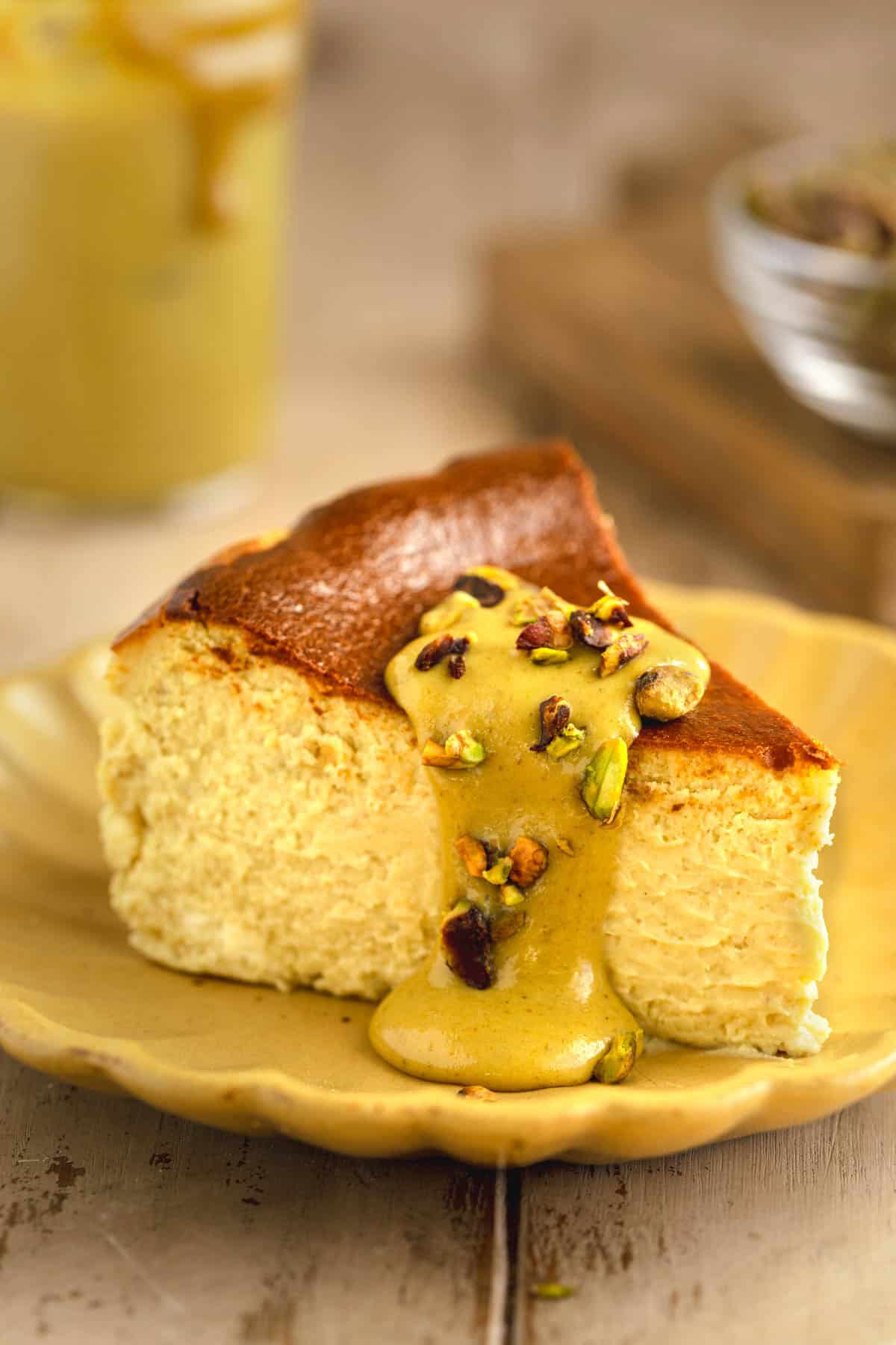 Pistachio Basque Cheesecake slice on a plate topped with pistachio cream and crushed pistachios.