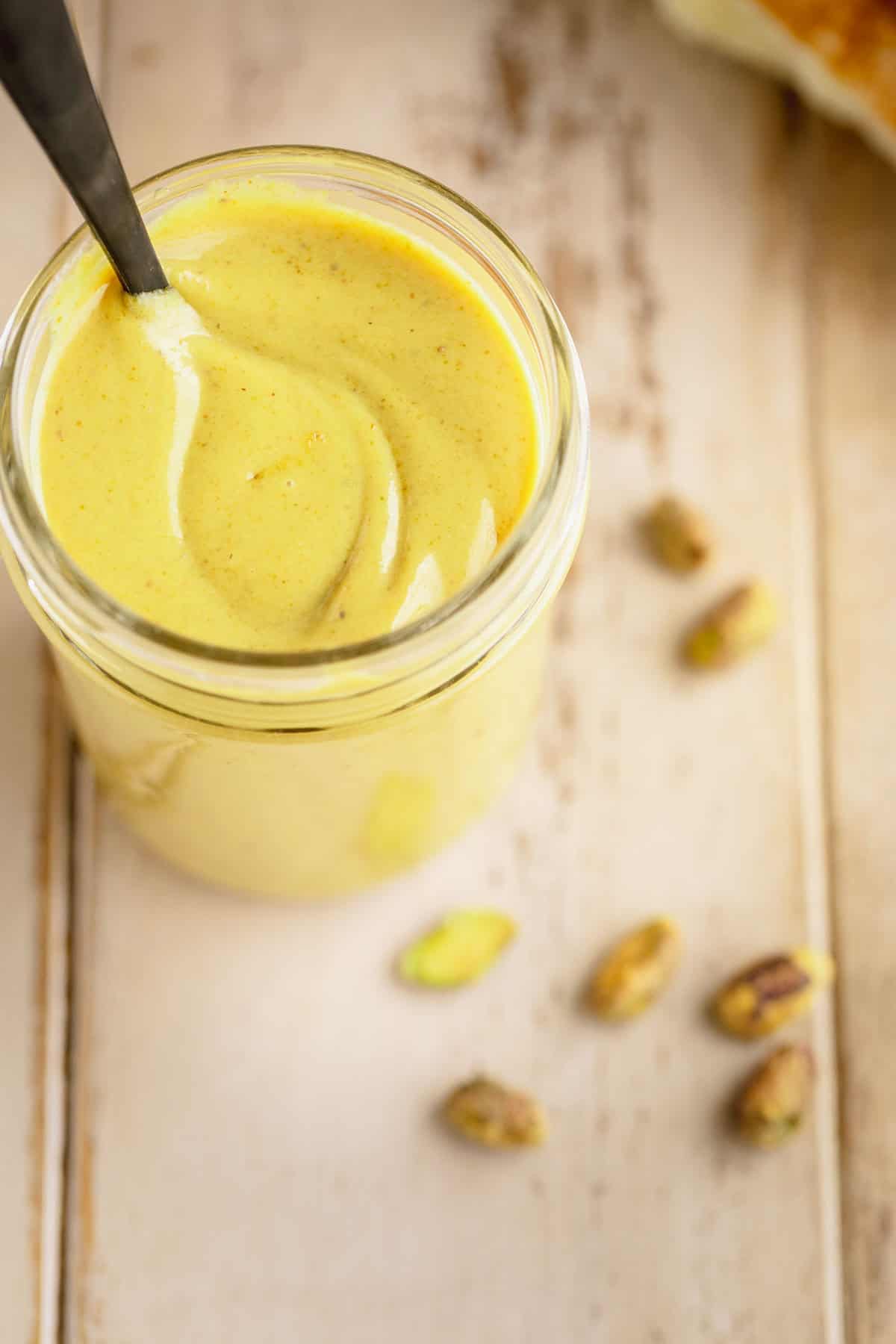 Pistachio cream in a jar with a spoon and a swirled top.