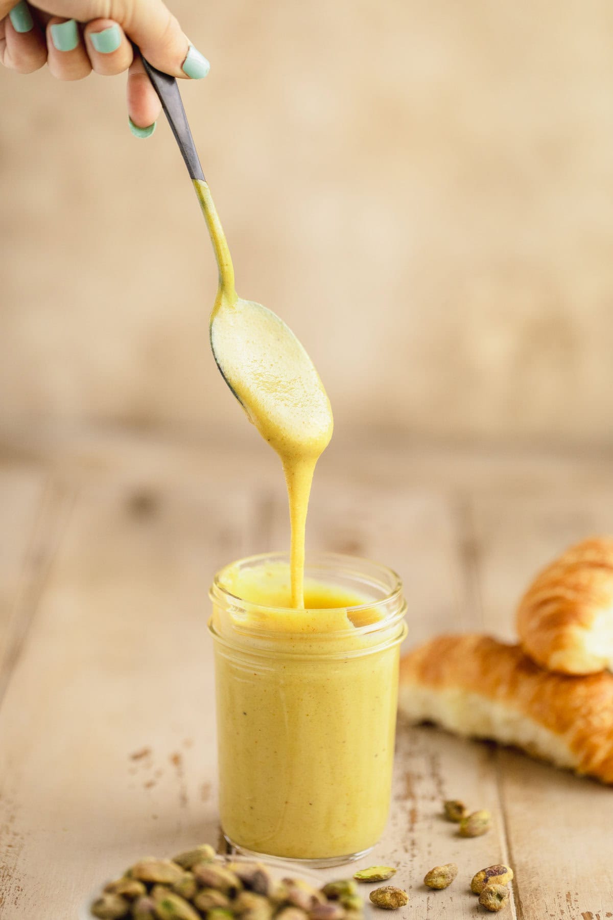 Pistachio cream being drizzled from a spoon into a full jar full.