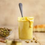 Pistachio cream in a jar with a spoon and a little cream overflowing down the side.