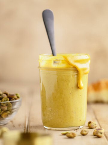 Pistachio cream in a jar with a spoon and a little cream overflowing down the side.