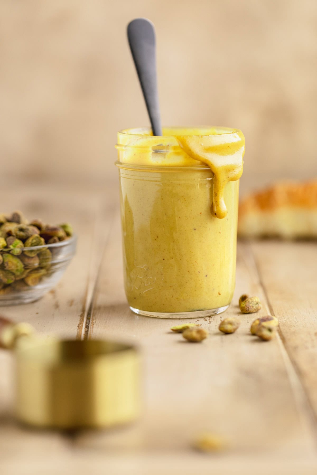 Pistachio cream in a jar wit a spoon next to a bowl of pistachios.